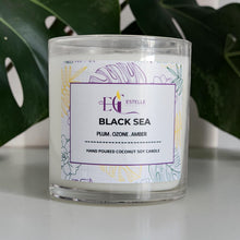 Load image into Gallery viewer, Black Sea Candle with a label on a white surface with green leaves in the background. Plum ozone Amber