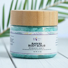 Load image into Gallery viewer, Jar of Black Sea Body Scrub with a natural cork lid on a light surface with green leaves in the background. Our sugar scrubs are formulated with luxurious ingredients, The sugar granules delicately exfoliate, while the shea butter, sunflower oil, and apricot kernel oil work together to hydrate and moisturize
