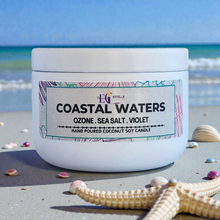Load image into Gallery viewer, Candle jar labeled 'Coastal Waters' on a beach with ocean in the background