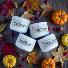 Load image into Gallery viewer, Four containers of different scented candles on a wooden surface with autumn leaves pumpkins. Pumpkin chai, harvest festival, black currant, apples and burbon