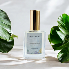 Load image into Gallery viewer, This image features one elegantly designed bottle of Eau De Parfum, with gold caps. The bottles are labeled  and are presented on a wooden surface with large green leaves in the background, enhancing the natural and sophisticated appeal of the products.