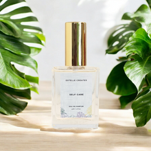 Load image into Gallery viewer, This image features one elegantly designed bottle of Eau De Parfum,with gold cap. and are presented on a wooden surface with large green leaves in the background, enhancing the natural and sophisticated appeal of the products.
