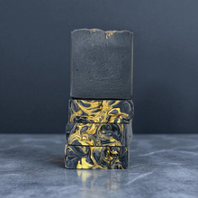 Load image into Gallery viewer, Three bars of soap with gold marbling on a dark gray background.  Indulge in our  handmadeartisan soap bar that transforms your daily routine into a luxurious escape.
