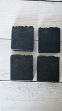 Load image into Gallery viewer, Four black square bars on a light wooden surface. Indulge in our  handmade artisan soap bar that transforms your daily routine into a luxurious escape.