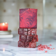 Load image into Gallery viewer, Stack of purple and pink marbled soap bars on a marble surface with a blurred candle in the background.  Indulge in our  handmade artisan soap bar that transforms your daily routine into a luxurious escape.
