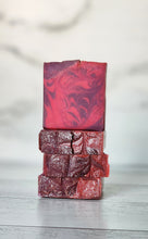 Load image into Gallery viewer, Stack of pink and purple marbled soap bars on a light wooden surface. Indulge in our  handmade artisan soap bar that transforms your daily routine into a luxurious escape.